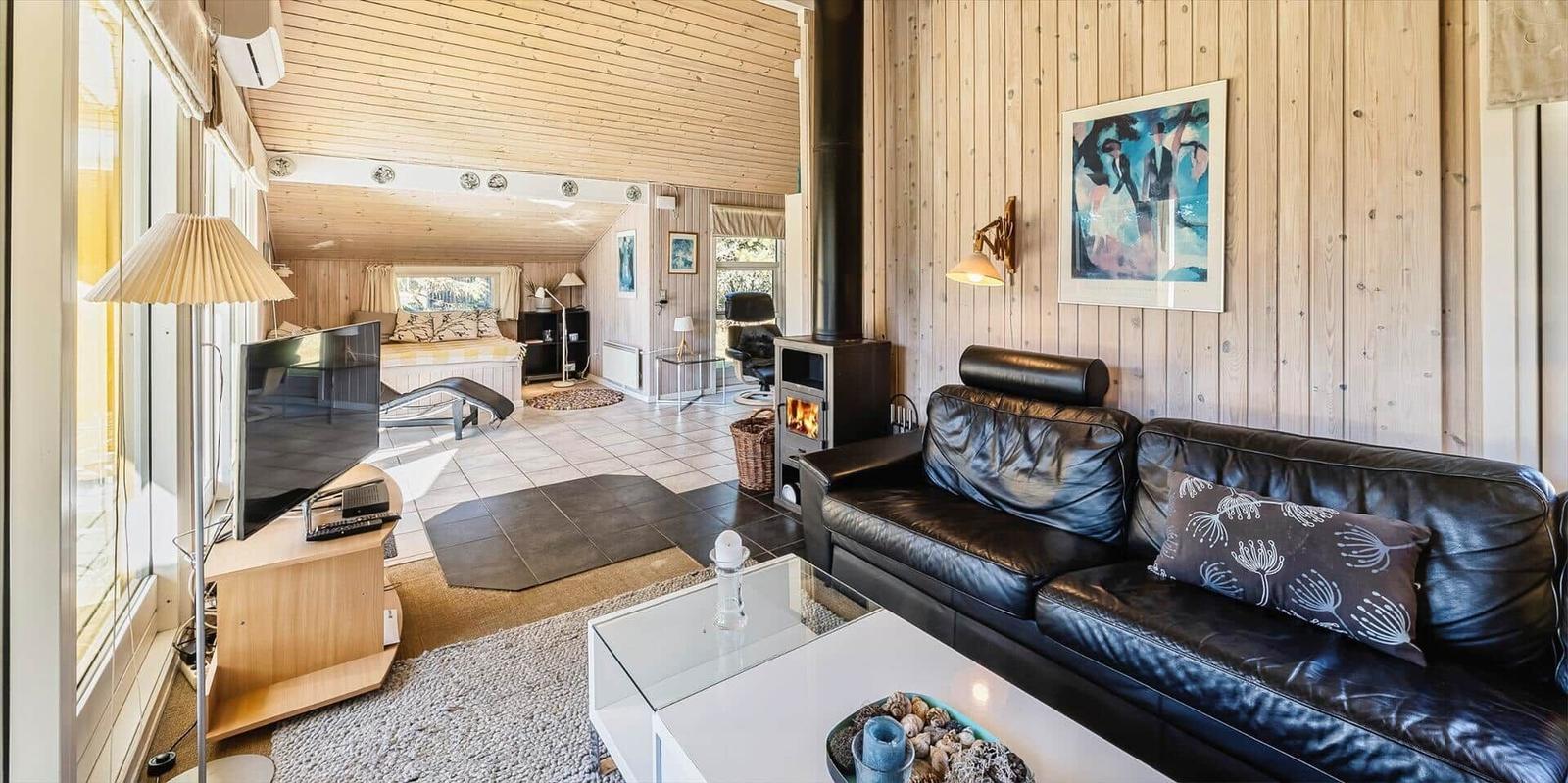 Wohnzimmer mit Ledersofa, Kamin und TV. Holzwände und Blick in Schlafzimmer.