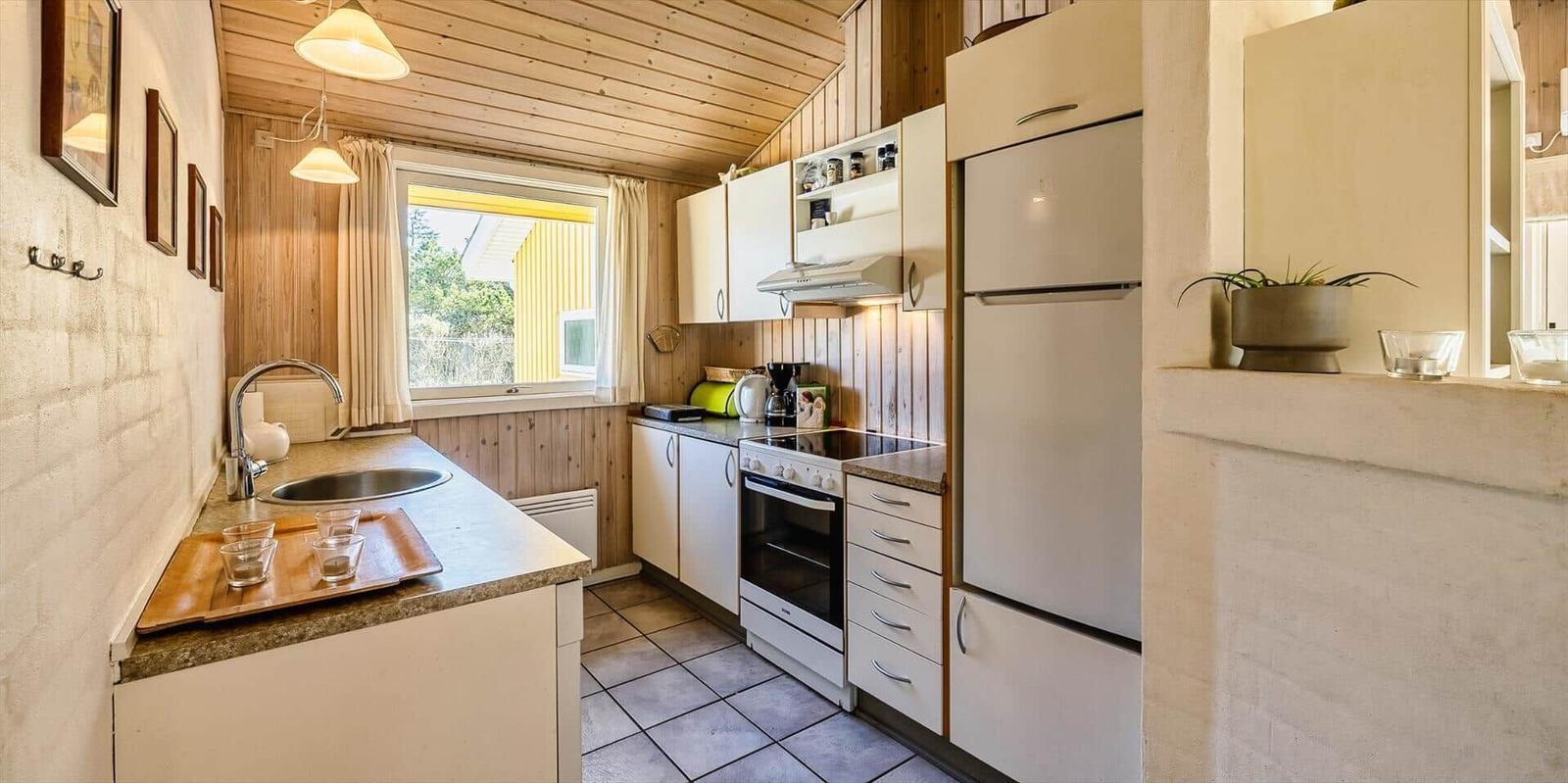 Küche mit Arbeitsplatte, Spüle, Kühlschrank und Herd. Holzwände und Fenster mit Blick.