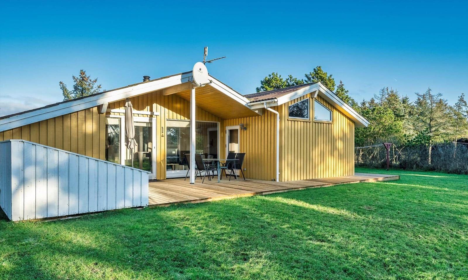 Ein gelbes Haus mit Terrasse und Garten. Es hat eine Satellitenschüssel und große Fenster.