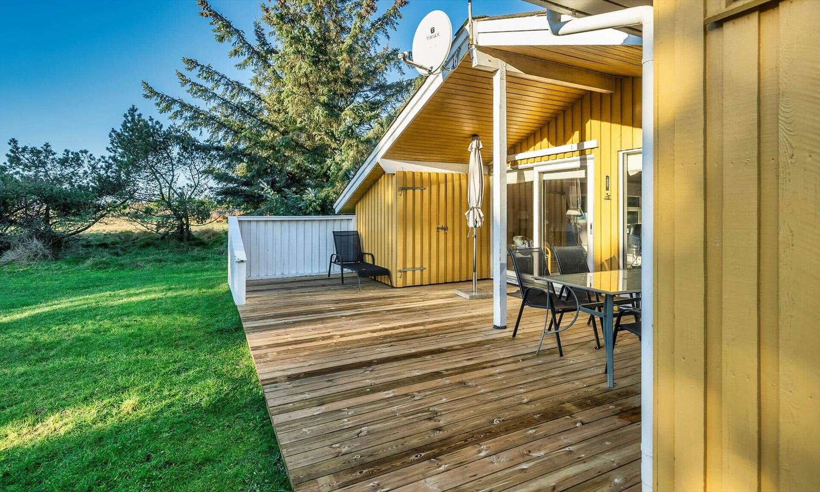 Holzterrasse mit Tisch, Stühlen und Sonnenschirm neben gelbem Haus.
