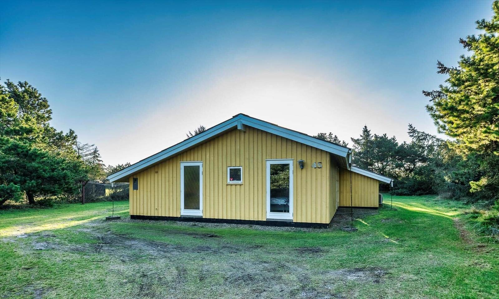 Gelbes Holzhaus mit weißen Türen und Fenstern, umgeben von Gras und Bäumen.