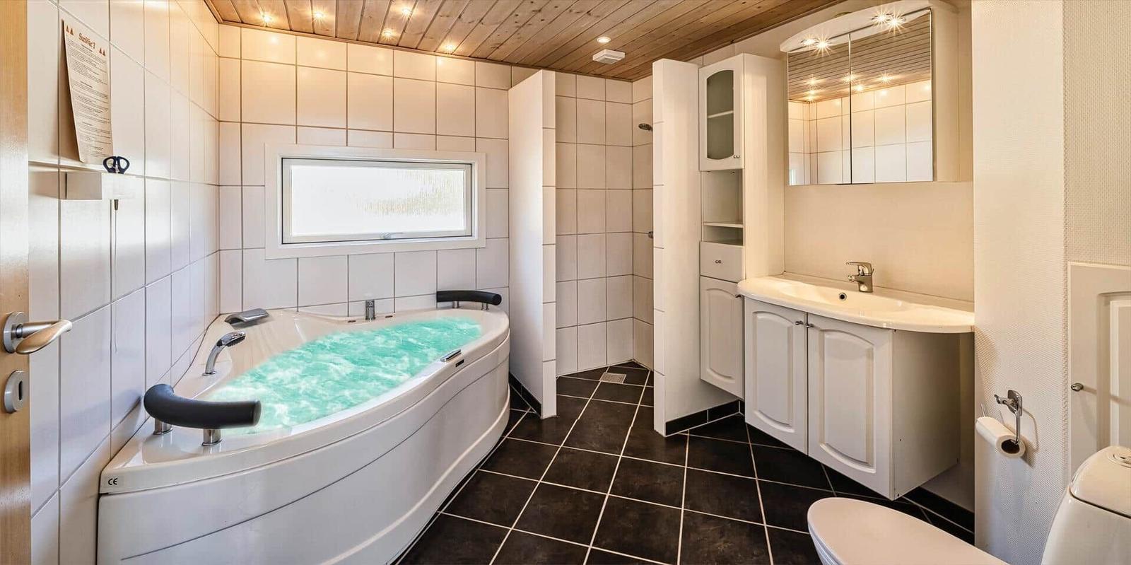 Badezimmer mit Whirlpool, Waschbecken und Toilette. Holzdecke und Fliesenboden.