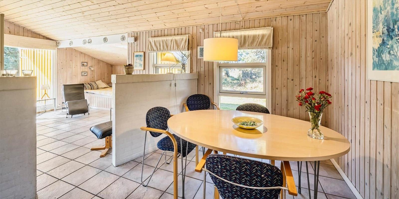Esszimmer mit runden Tisch und Stühlen, Holzwände, Fenster und Blumen.