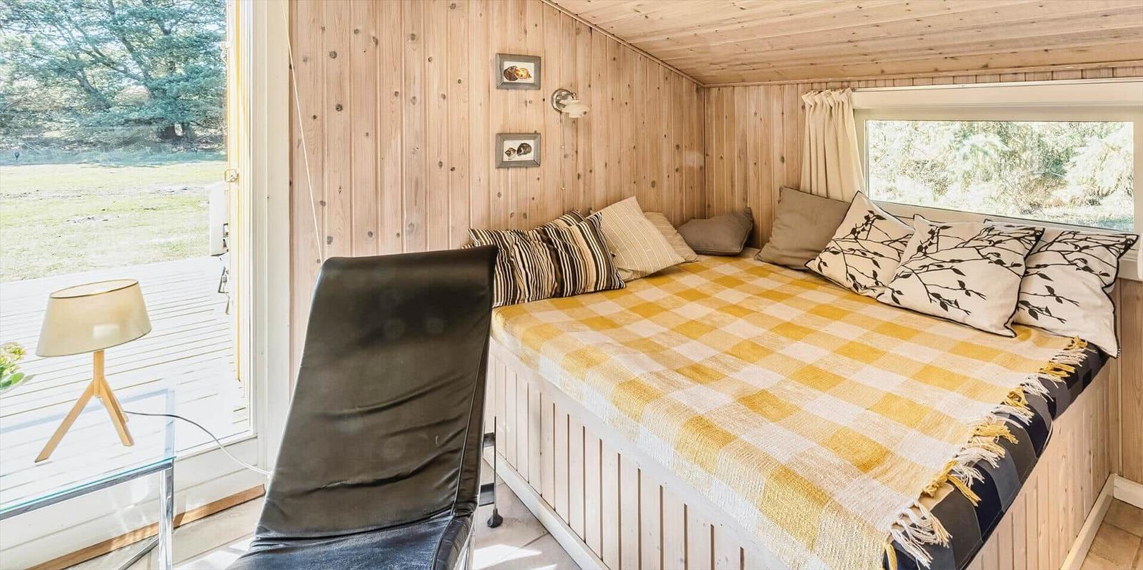Schlafzimmer mit Holzwand, Bett mit gelbem Decken und Fensterblick.