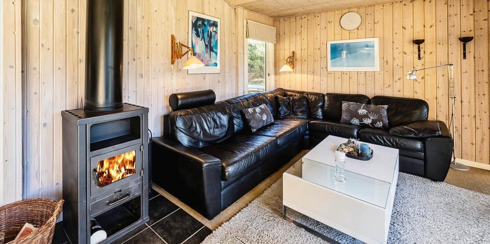 Wohnzimmer mit Holzwand, schwarzer Ledercouch, Kamin und Glas-Tisch.
