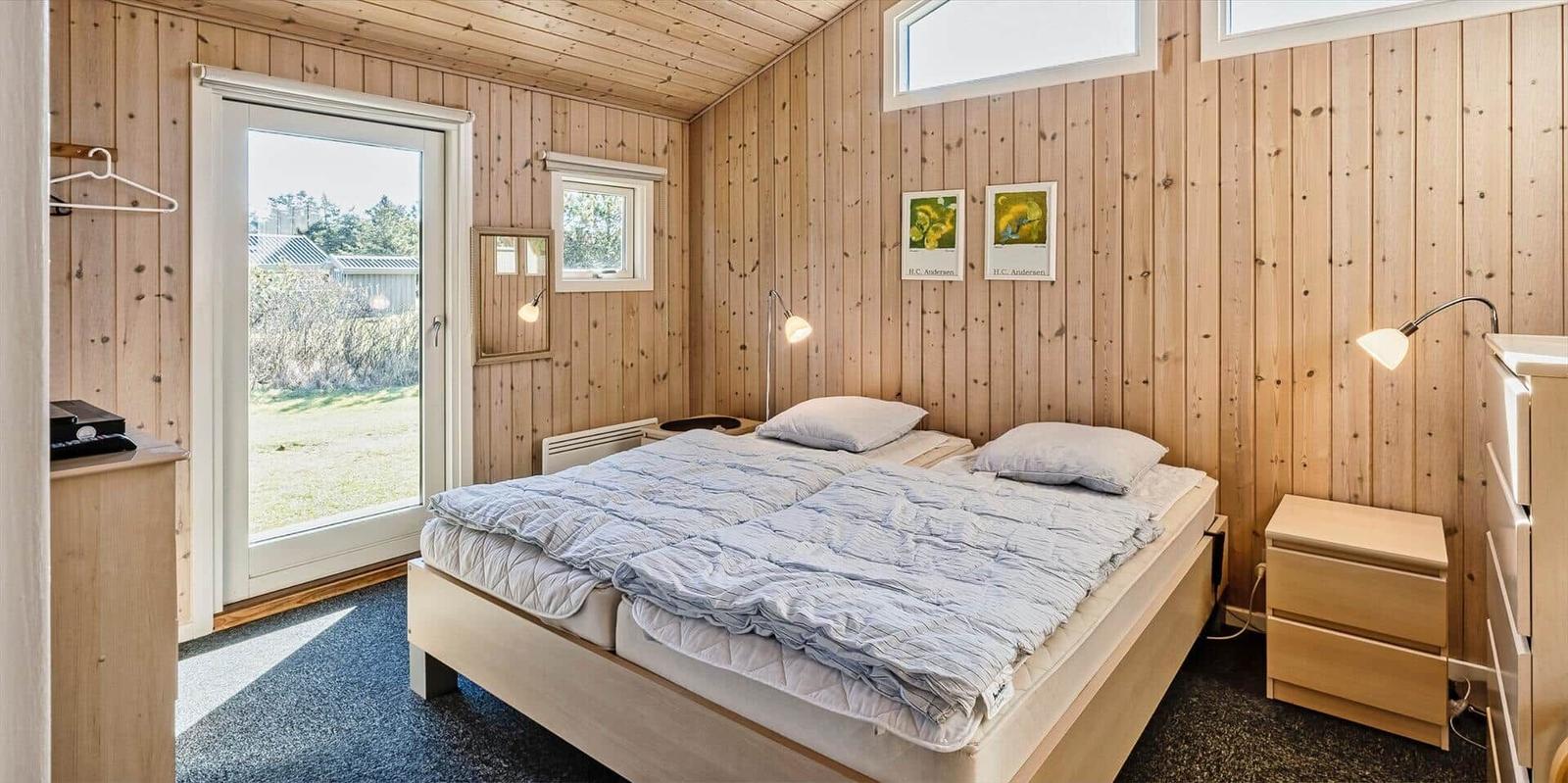 Schlafzimmer mit Holzwand, Bett, Nachttisch und Tür zum Garten.