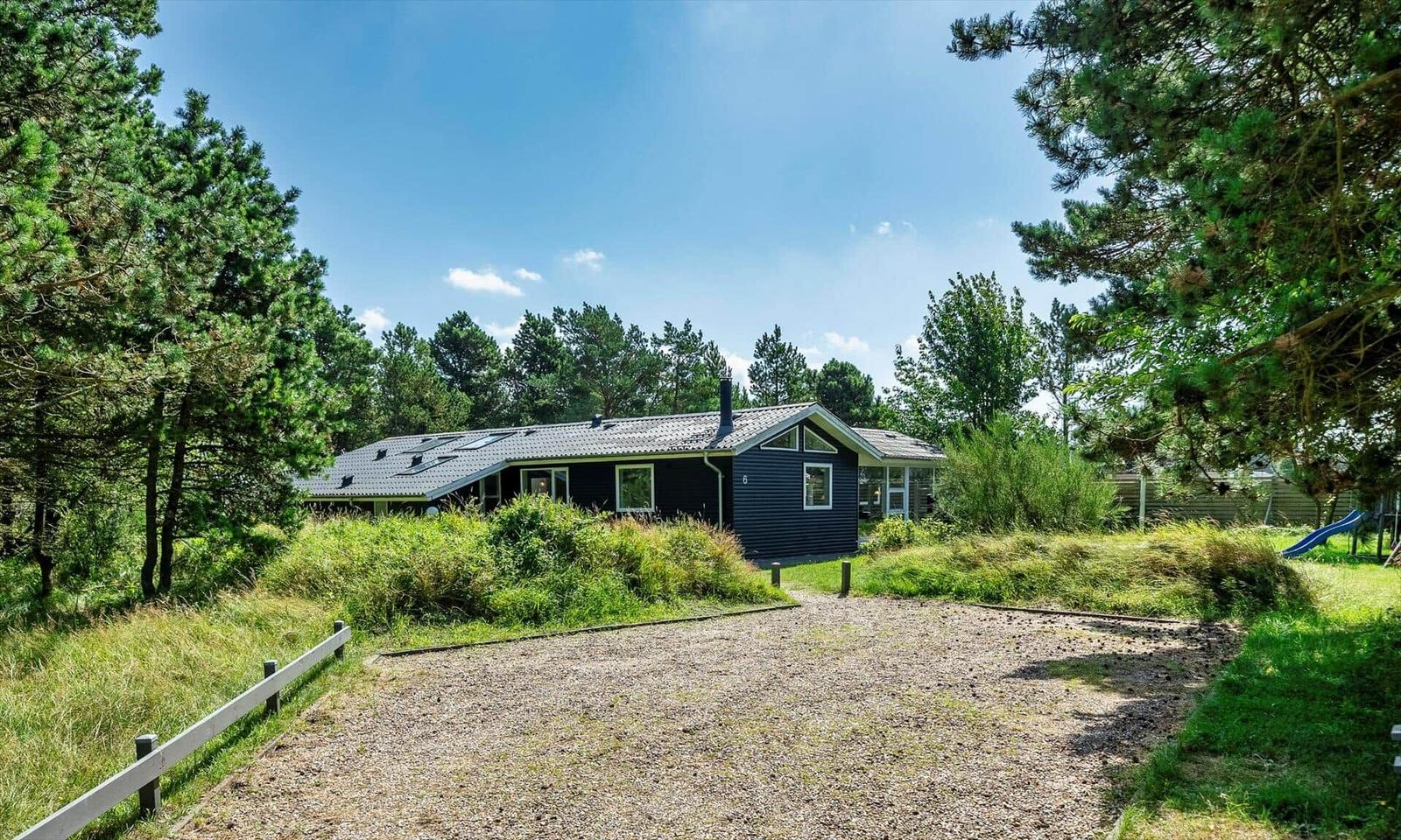 Ein dunkelblaues Haus mit Dachgauben steht inmitten von Bäumen und Gras.