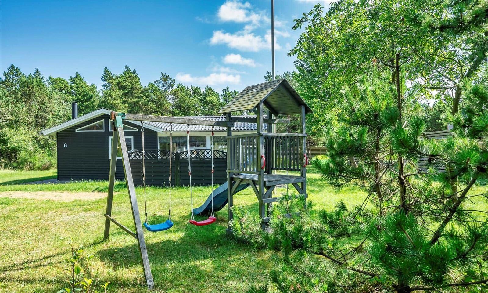 Schwarzes Ferienhaus mit Spielplatz im Grün.