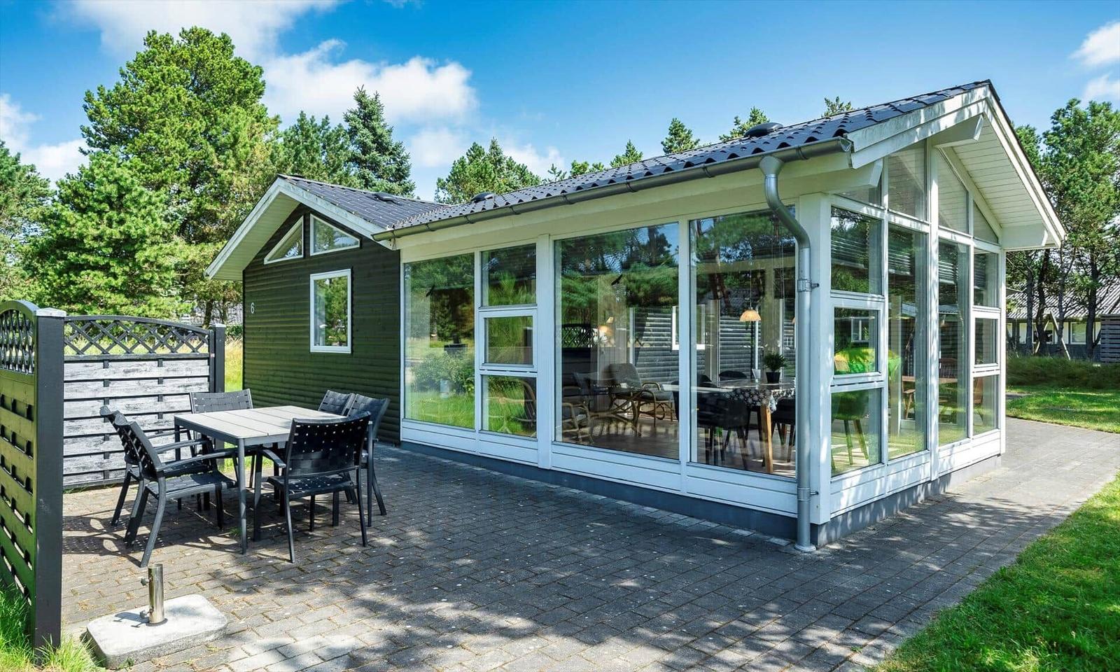 Moderne Ferienhaus mit großem Glasbereich und Terrasse mit Tisch und Stühlen.