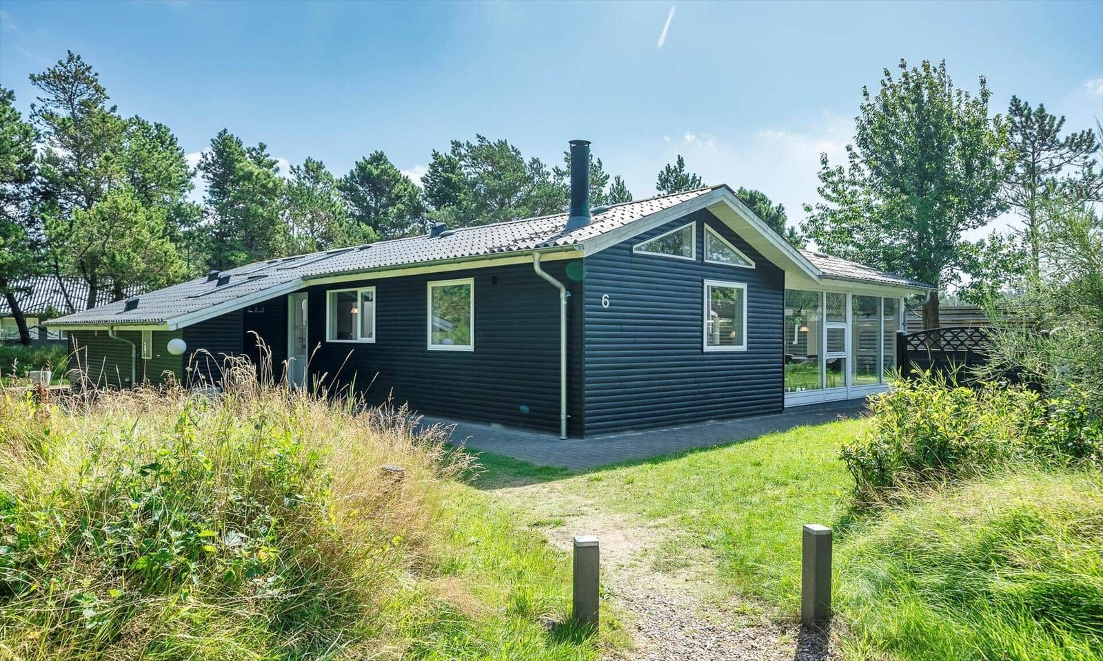 Ein schwarzes Ferienhaus mit Holzfassade und großem Glasbereich. Umgeben von Gras und Bäumen.