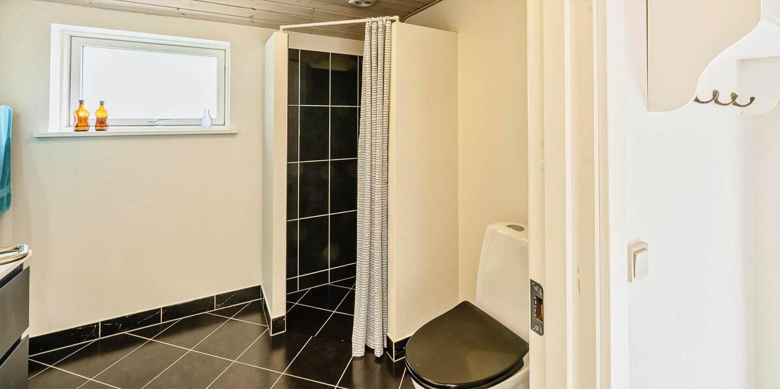 Badezimmer mit Dusche, Toilette und Fenster mit Flaschen auf Sims.