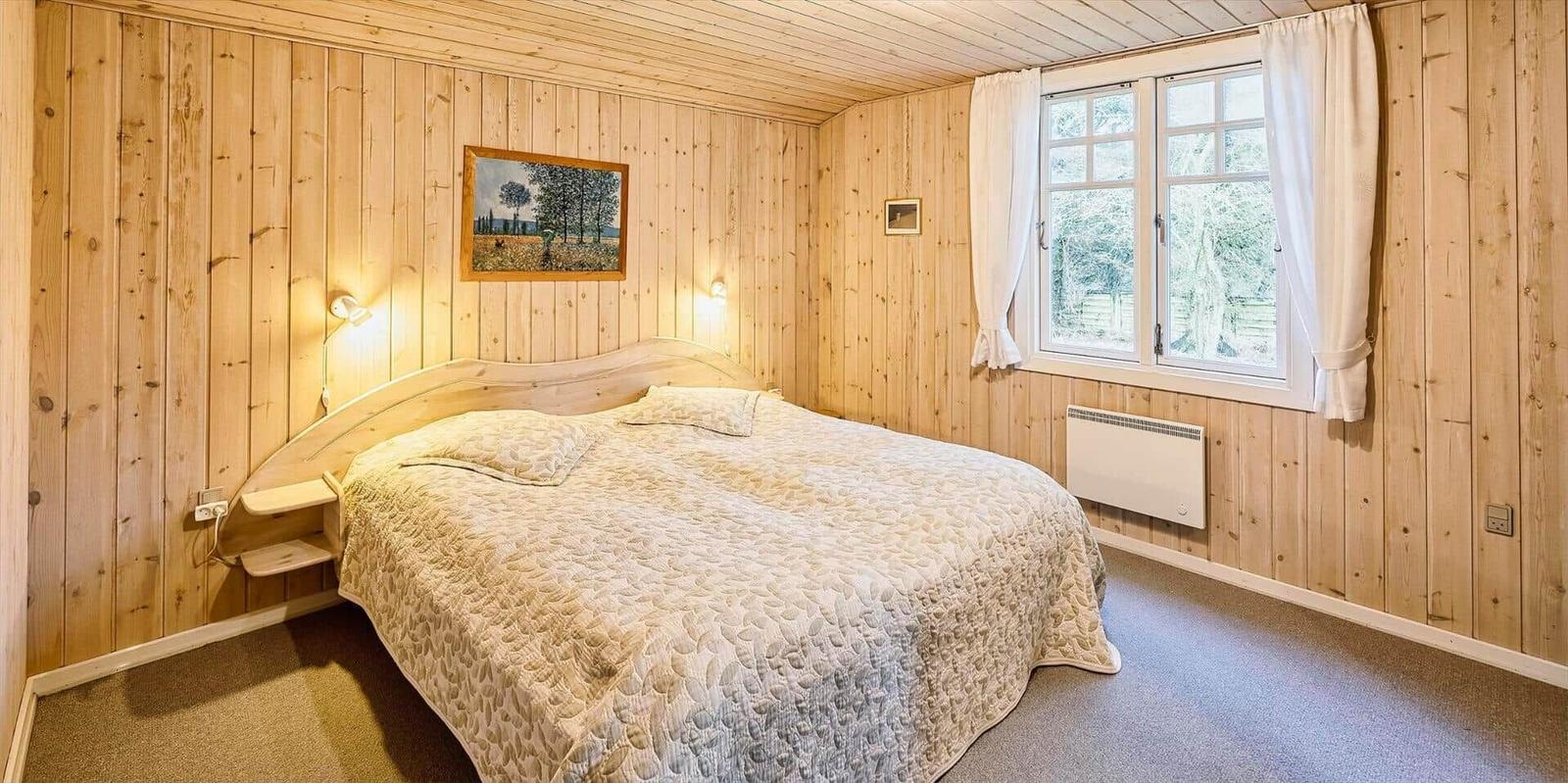 Schlafzimmer mit Holzwand, Bett und Fenster mit Blick auf Außenbereich.