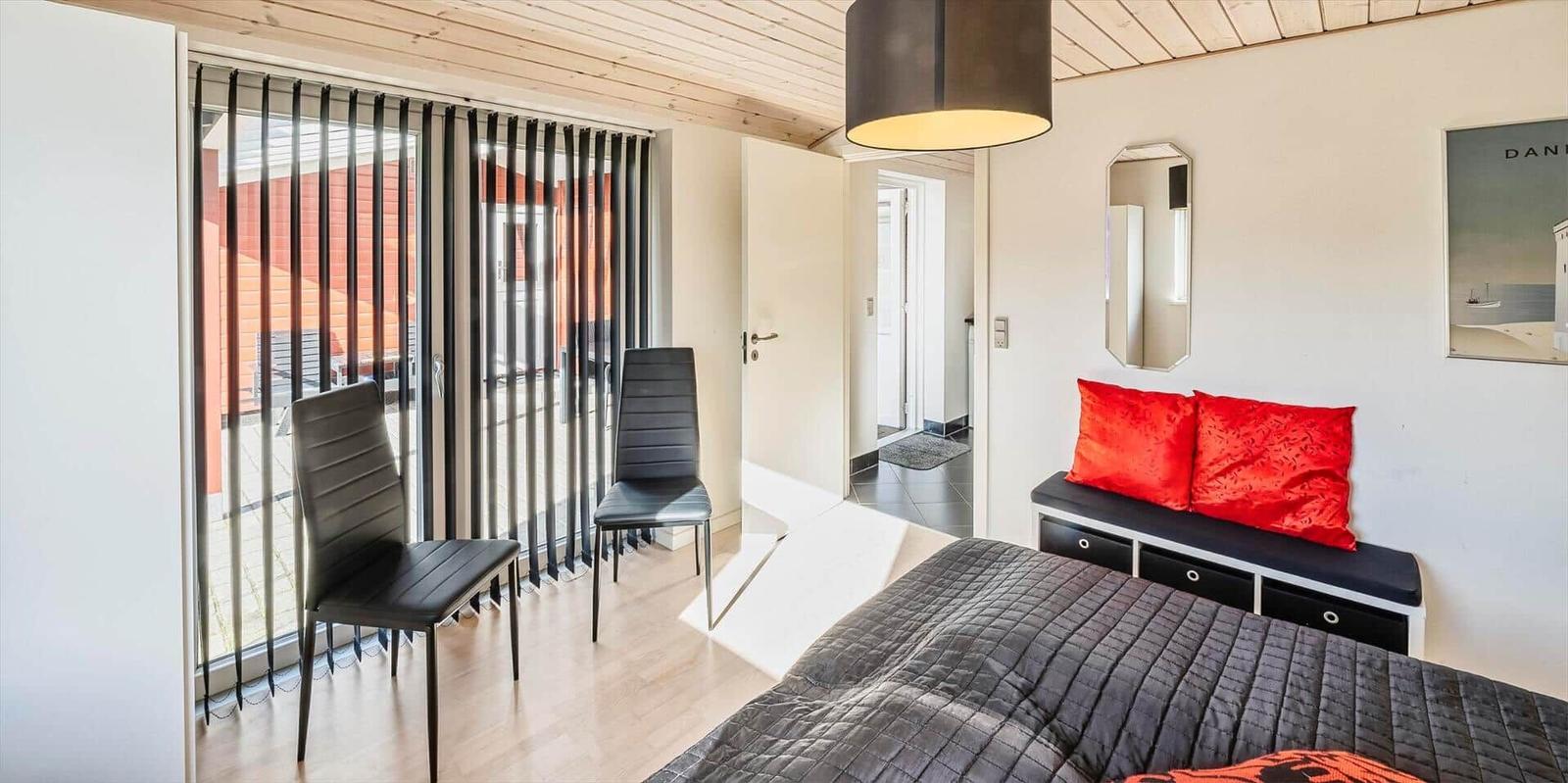 Schlafzimmer mit Bett, Sitzbank, zwei Stühlen und Blick auf Balkon.