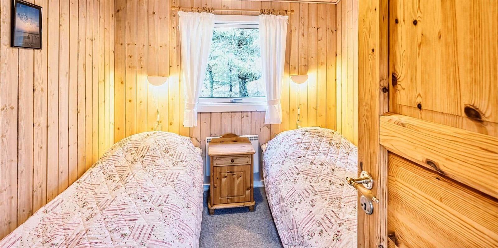 Zwei Betten mit gemusterten Bettdecken stehen in einem Raum mit Holzwänden und einem Fenster.