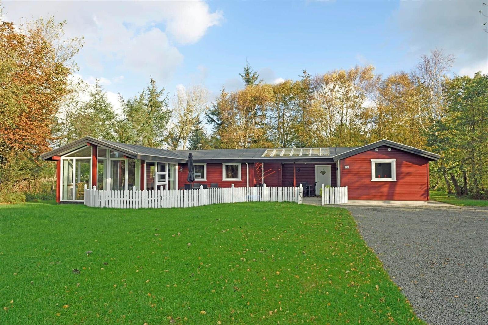 Rotes Haus mit weißem Zaun und grünem Rasen. Hinterhof mit Gartenmöbeln.
