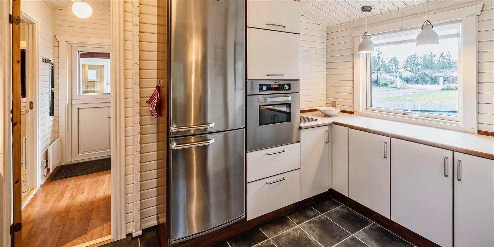 Küche mit Edelstahl-Kühlschrank und Backofen, weißer Arbeitsfläche und Fensterblick auf Grünfläche.