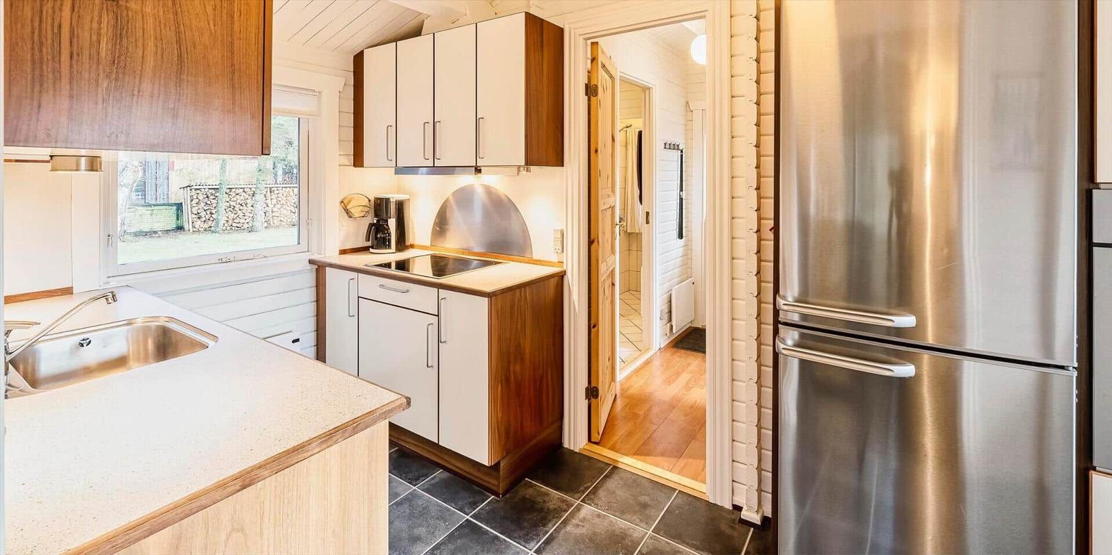 Küche mit Edelstahlkühlschrank und Holzschränken. Blick in das Badezimmer.