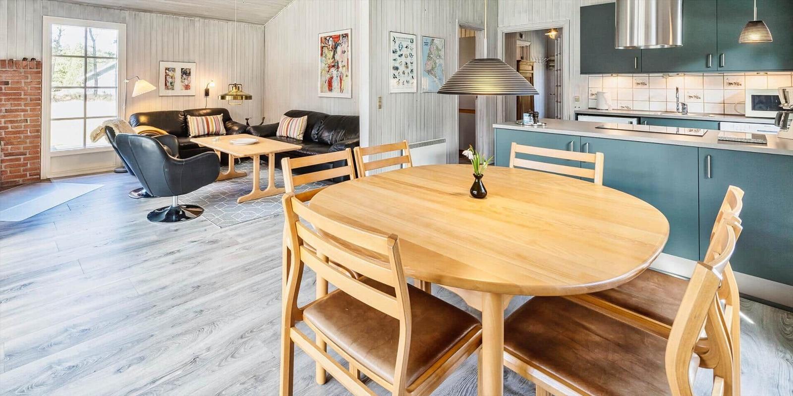 Essbereich mit Holztisch und Stühlen. Küche und Wohnzimmer im Hintergrund.