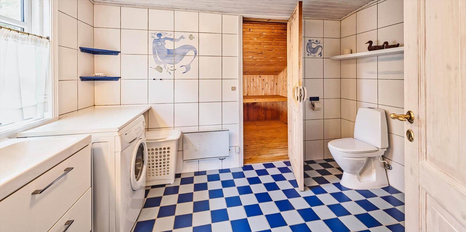 Badezimmer mit Sauna, Toilette, Waschmaschine und blau-weißem Bodenfliesenmuster.