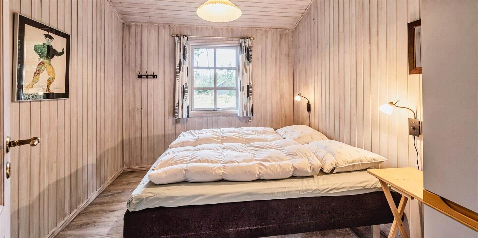 Schlafzimmer mit Holzwand, Bett, Fenster und Wandlampen.