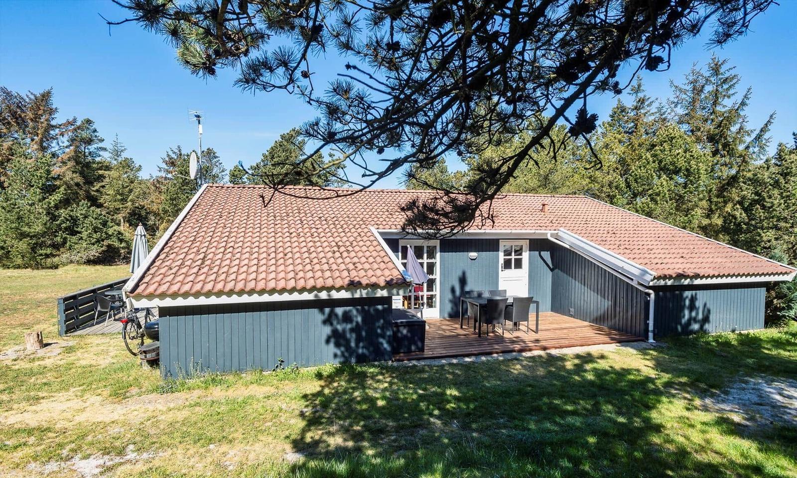 Ein Haus mit Terrasse, Tisch und Stühlen, umgeben von Bäumen und Gras.