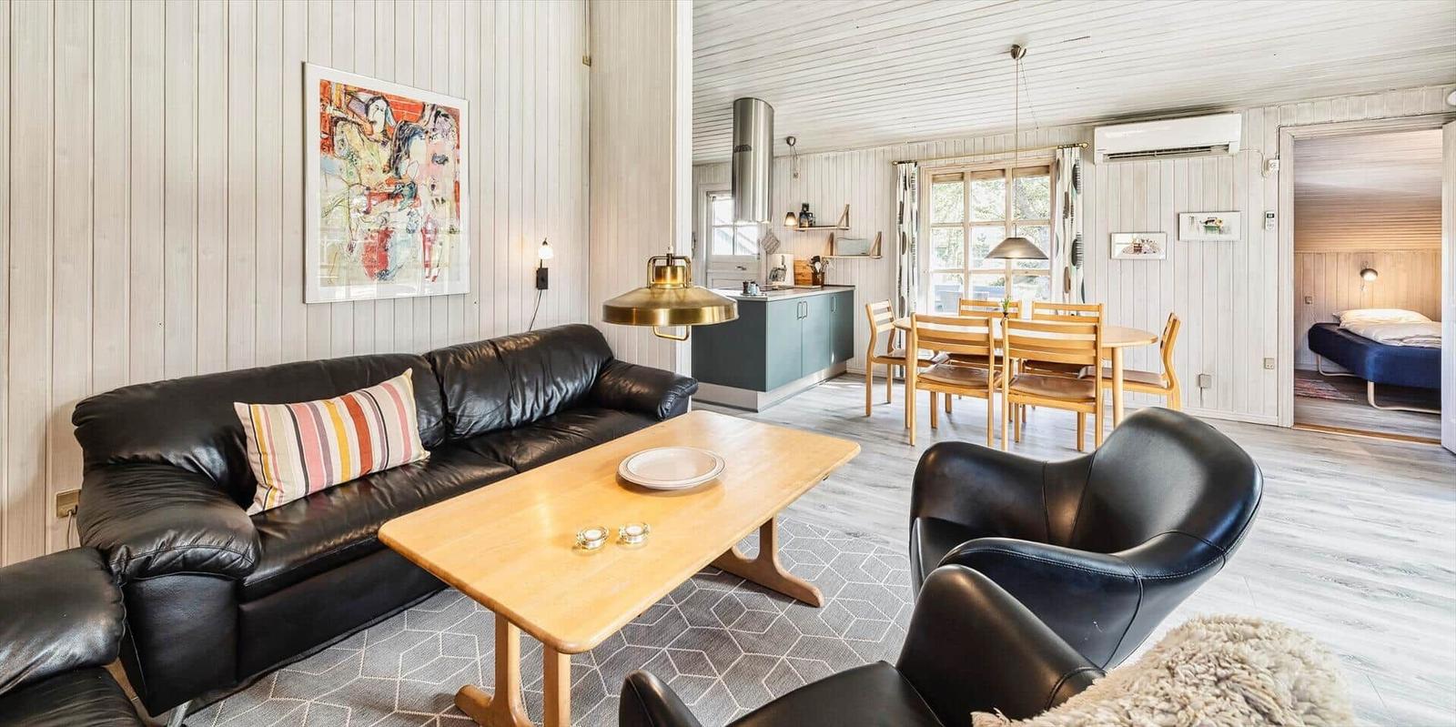 Wohnzimmer mit Sofa, Sessel und Esstisch. Küche und Schlafzimmer sind sichtbar.