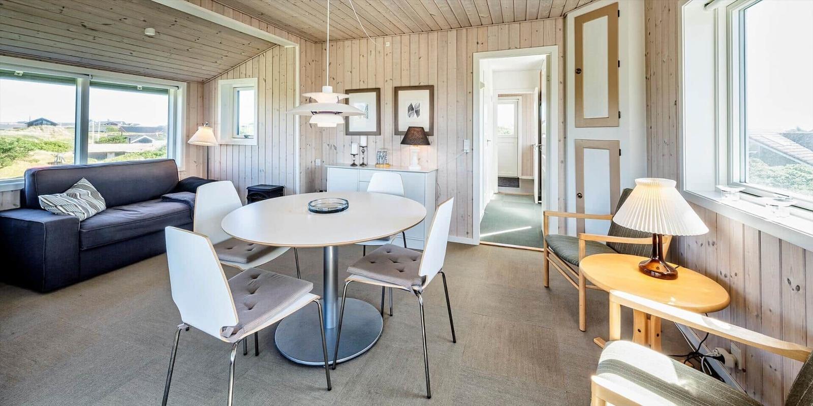 Wohn- und Essbereich mit Holzwänden, Sofa, runder Tisch und Stühlen.