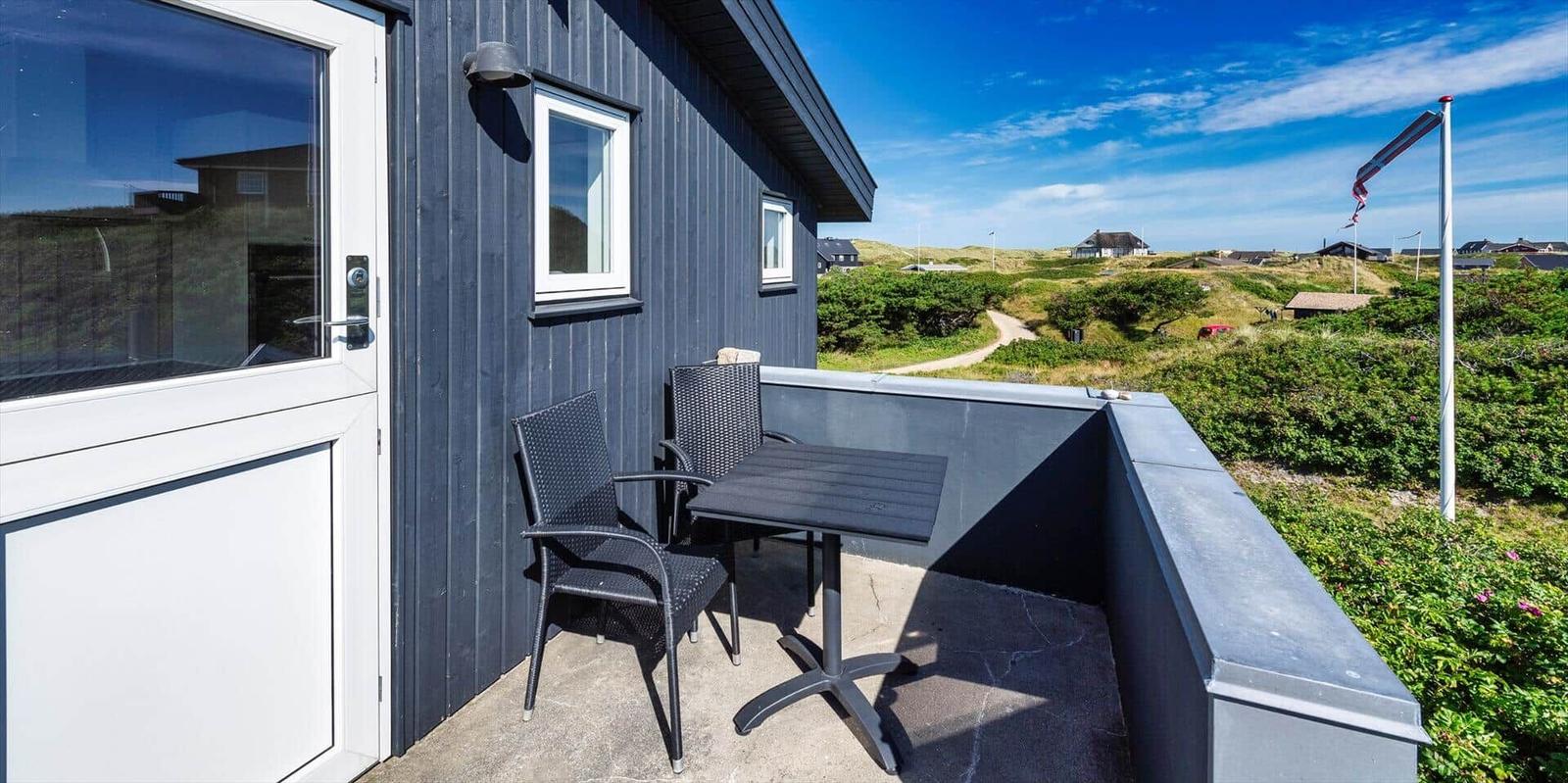 Terrasse mit Tisch und Stühlen vor einem dunkelblauen Haus mit Blick auf grüne Hügel.