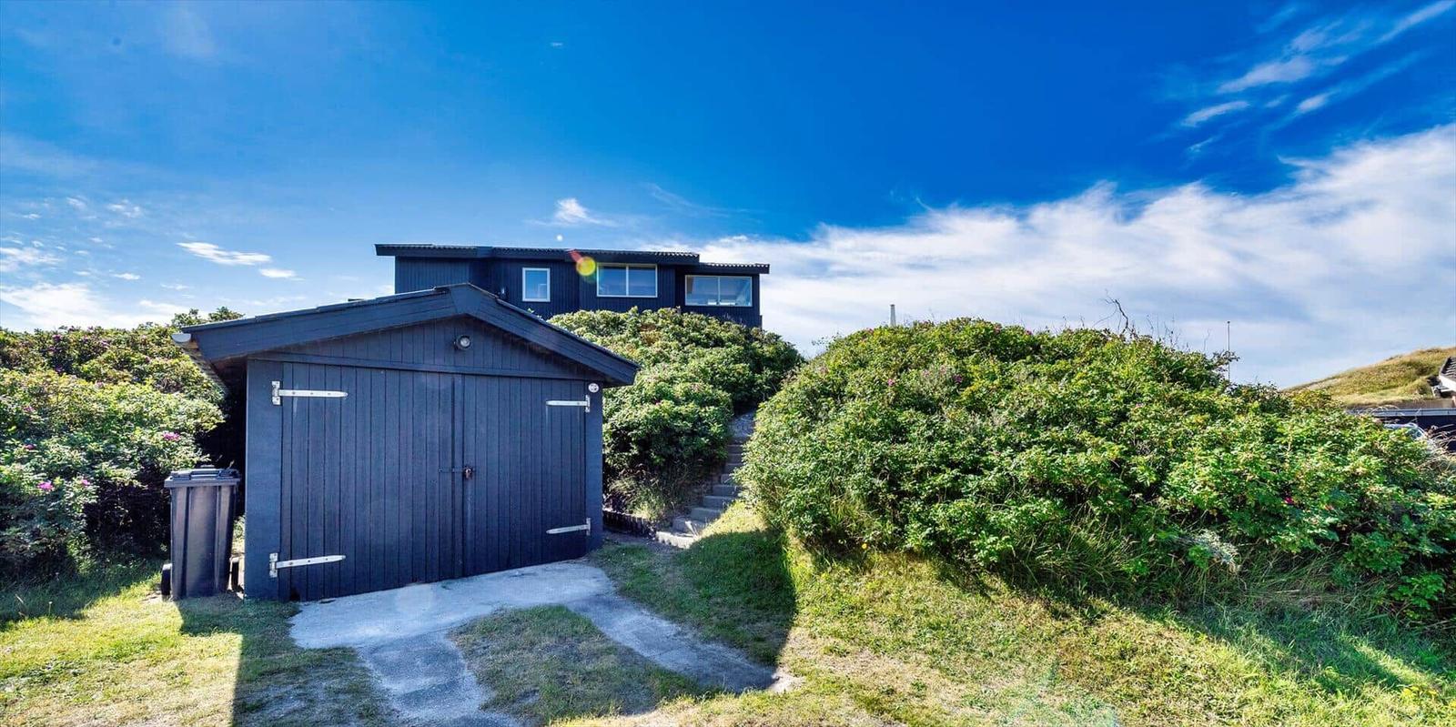 Schwarzes Haus mit Garage und Stufen durch Grünflächen unter blauem Himmel.