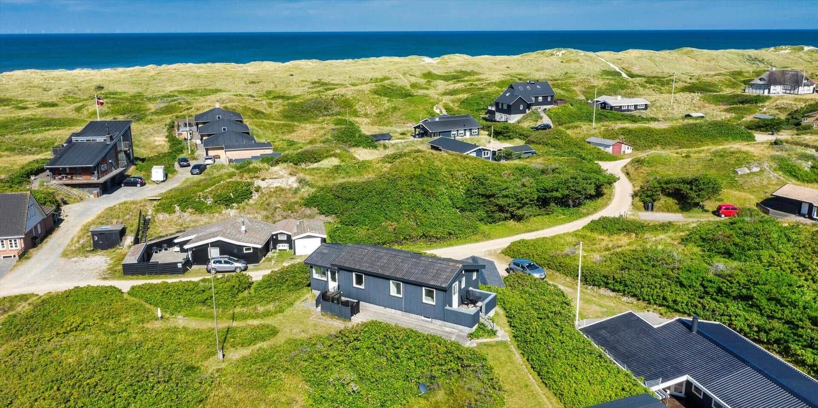 Meerblick auf eine grüne Dünenlandschaft mit mehreren Häusern und Fahrzeugen.