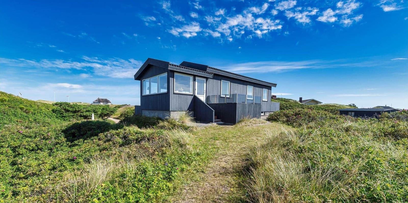 Moderne Strandhaus mit großem Fensterfront und grüner Umgebung.