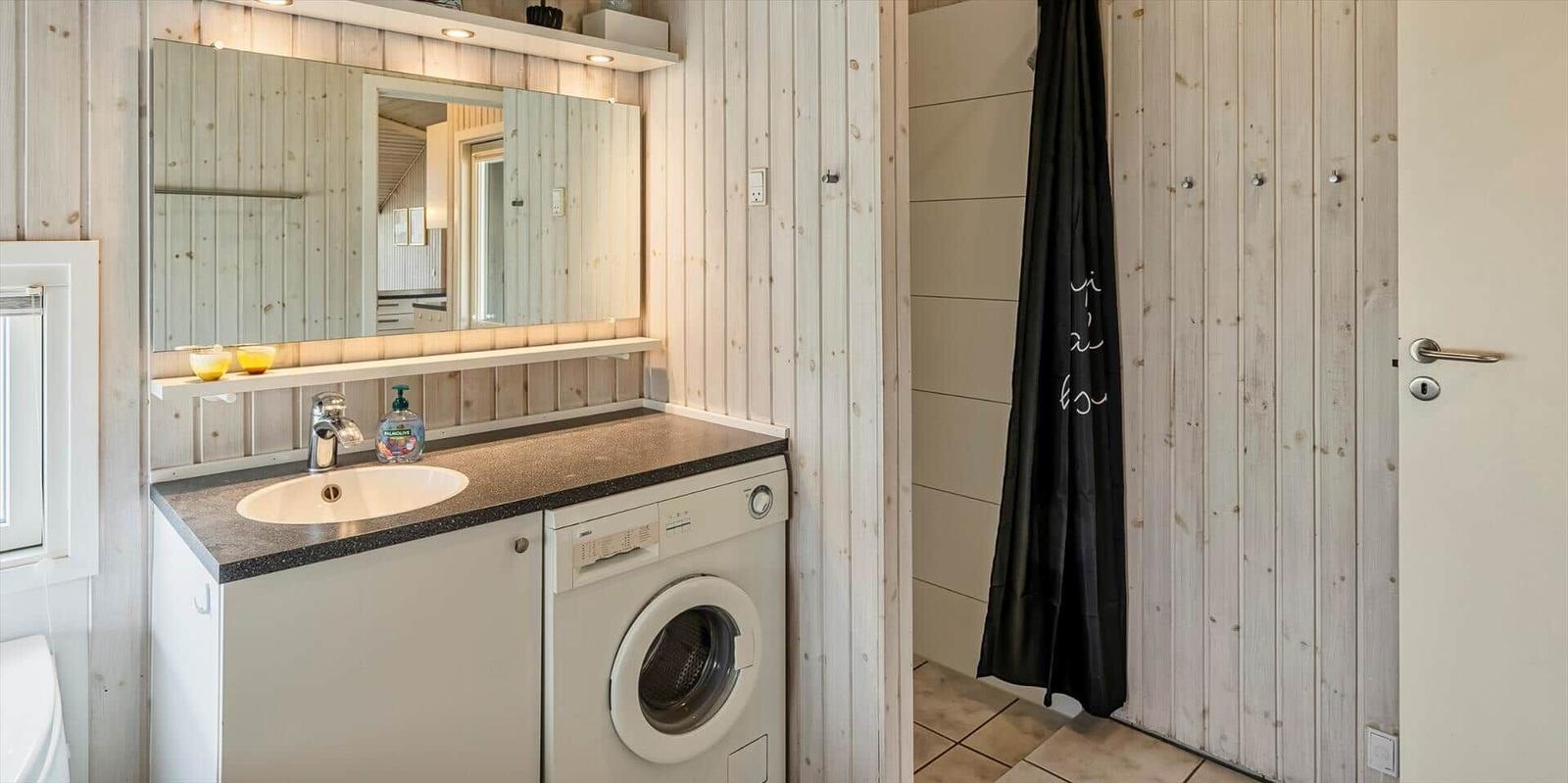 Badezimmer mit Waschmaschine, Spiegel und Duschvorhang.
