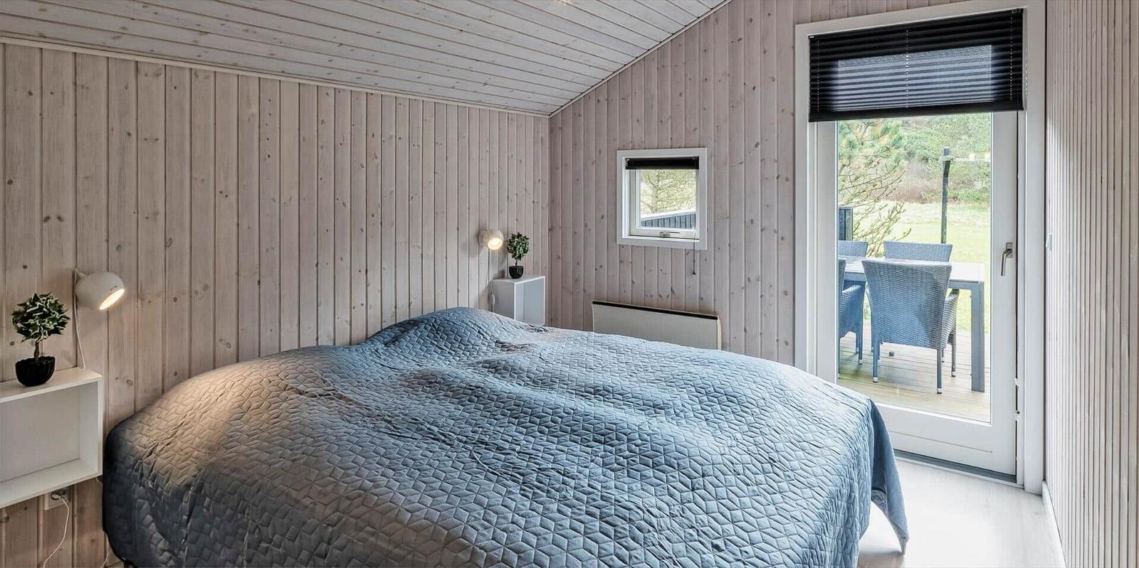 Schlafzimmer mit Bett, Holzwand und Terrassentür.