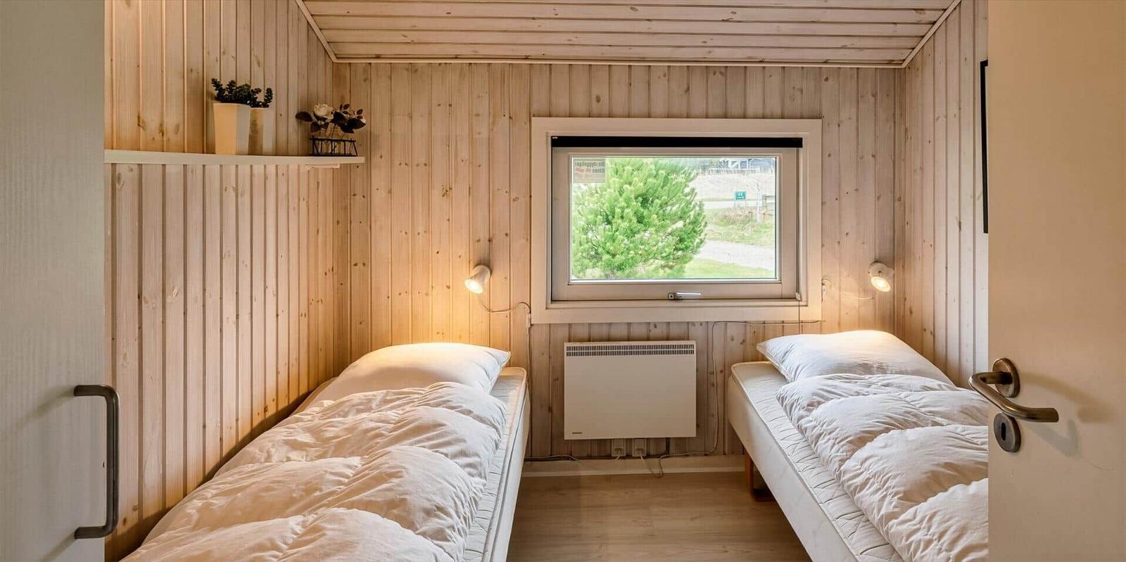 Zwei Einzelbetten in einem Holzraum mit Fenster und Heizung.