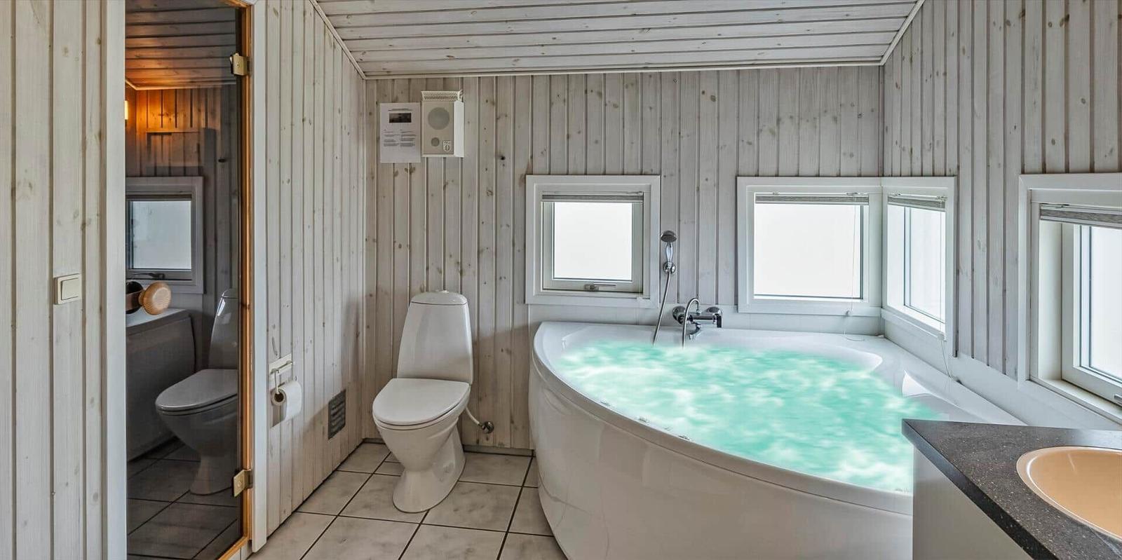 Bad mit Whirlpool, Toilette und Dusche. Holzwände und Fenster.