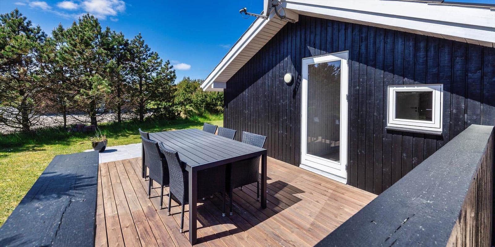 Terrasse mit Tisch und Stühlen vor einem Haus mit dunklem Holzverkleidung.