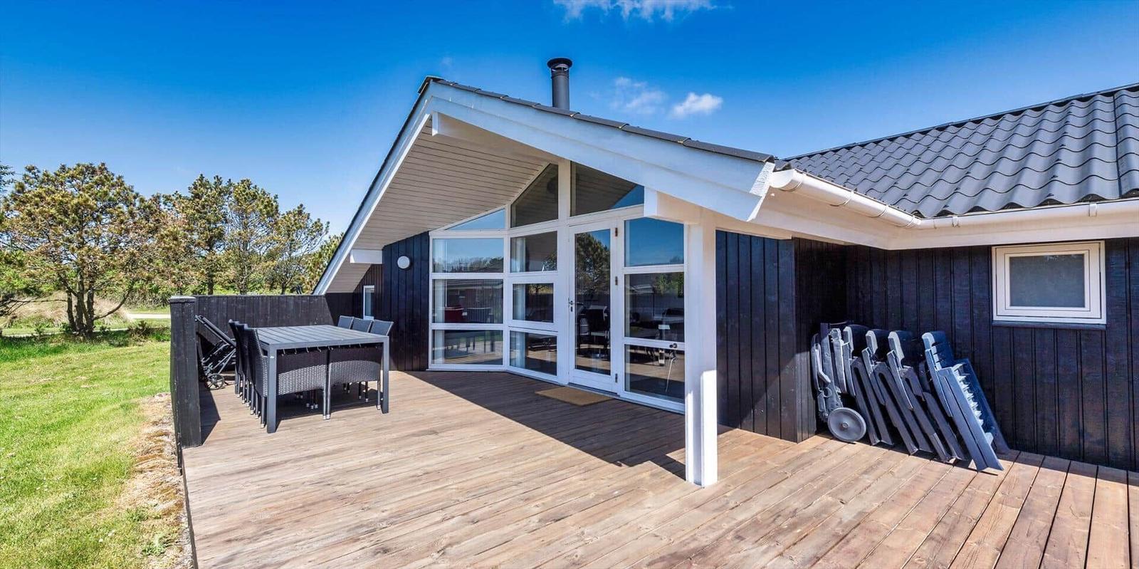Holzterrasse mit Tisch und Stühlen vor einem Haus mit großem Fenster.