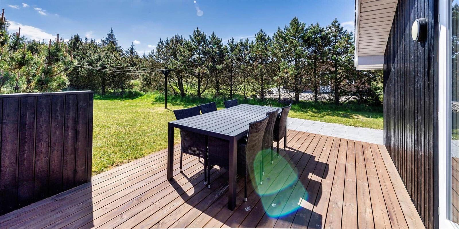 Terrasse mit Tisch und Stühlen, Blick auf grünen Rasen und Bäume.