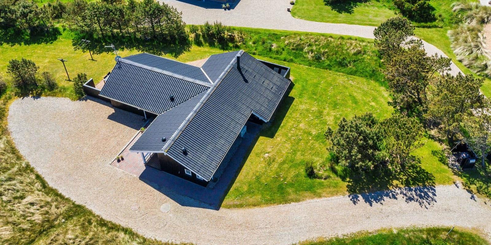 Modernes Haus mit dunklem Dach auf grünem Grundstück mit Bäumen und Kiesweg.