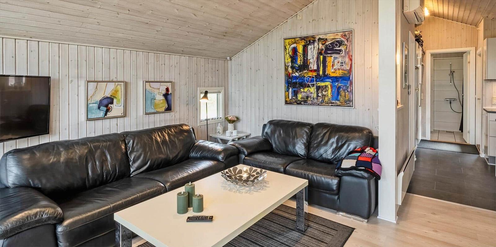 Wohnzimmer mit zwei schwarzen Ledersofas, Tisch und Wandbildern.