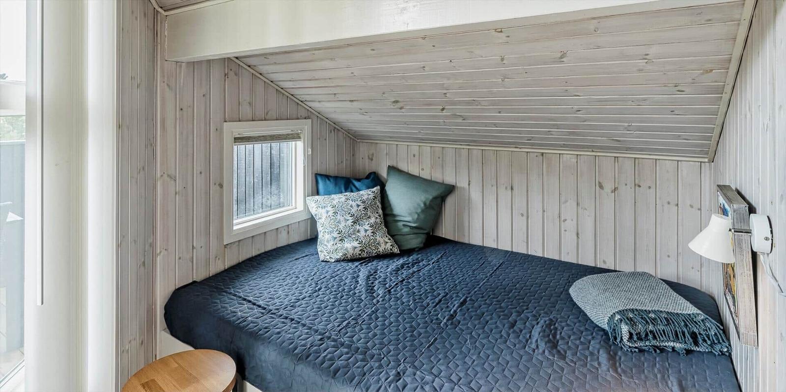 Schlafzimmer mit Bett, Fenster und Holzwandverkleidung