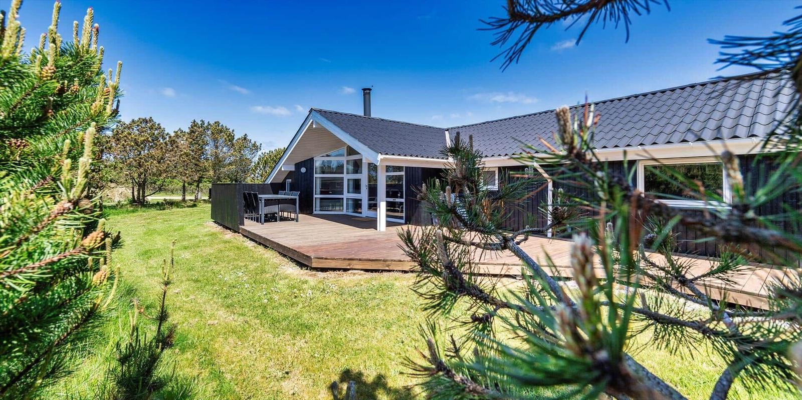 Modernes Ferienhaus mit Holzterrasse und Blick auf grünen Garten.