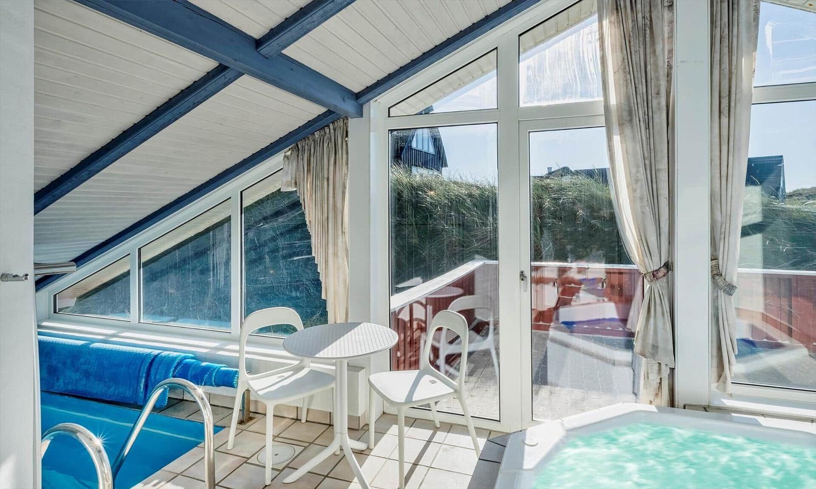Innenbereich mit Pool, Whirlpool und Sitzgelegenheit. Große Fenster bieten Blick auf Außengelände.