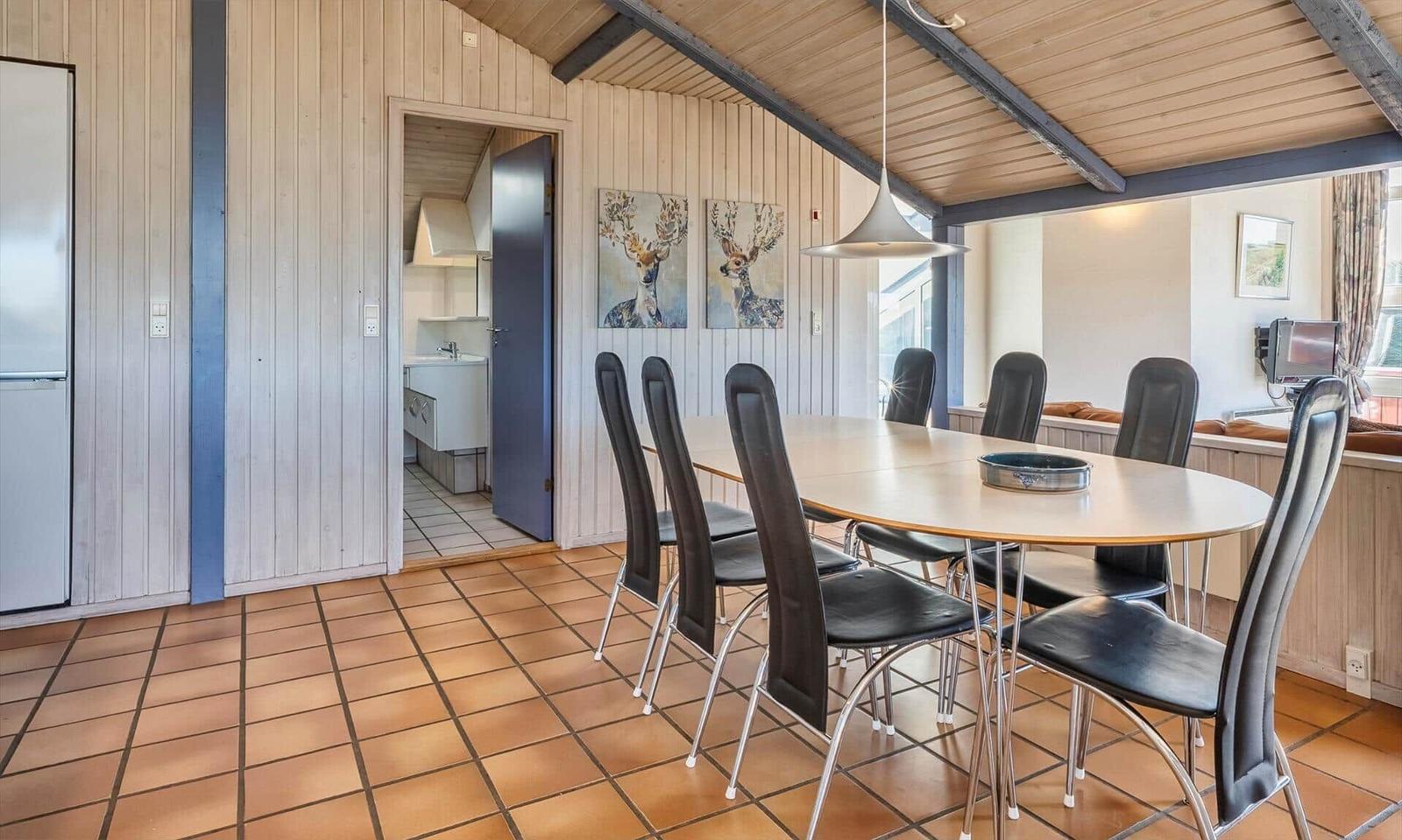 Esszimmer mit ovaler Tisch und sechs Stühlen, Holzwand und Küchenbereich sichtbar.