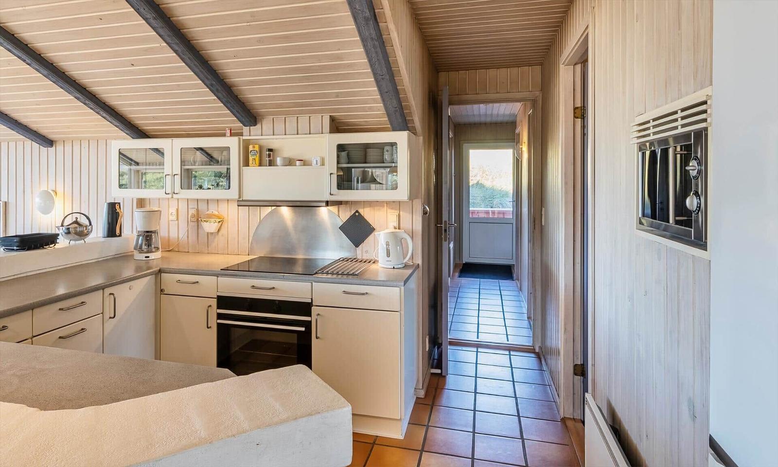 Küche mit Holzwand und integriertem Ofen. Tür führt zu Terrasse.