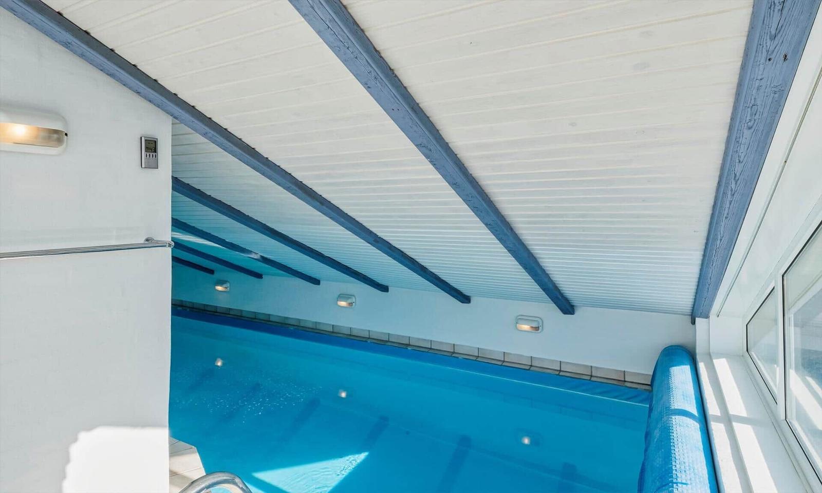 Innere Schwimmhalle mit blauem Wasser und Holzbalken an der Decke.