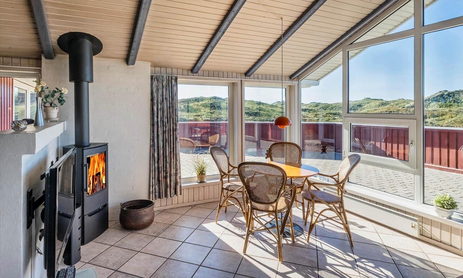 Ein Raum mit Kamin, Esstisch und großem Fensterblick auf die Landschaft.