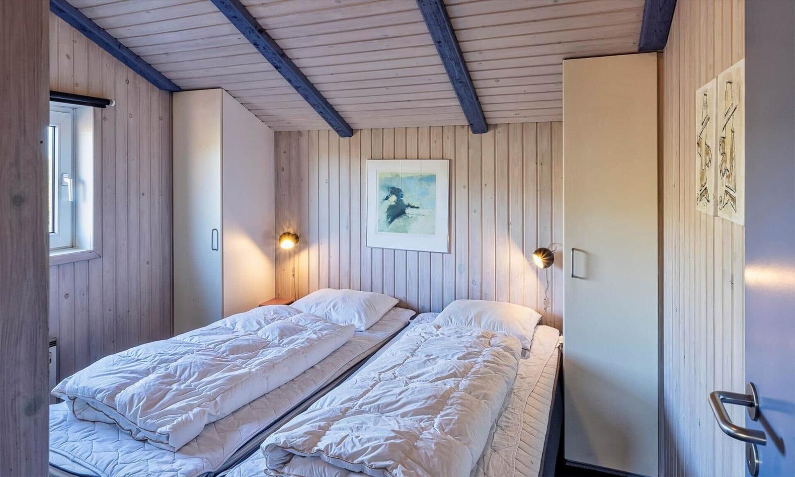 Zimmer mit zwei Betten, Holzwand und Deckenbalken, Wandbild und Nachttischlampen.