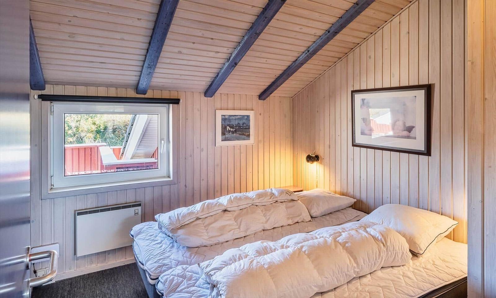 Schlafzimmer mit Bett, Fenster und Holzwandverkleidung.