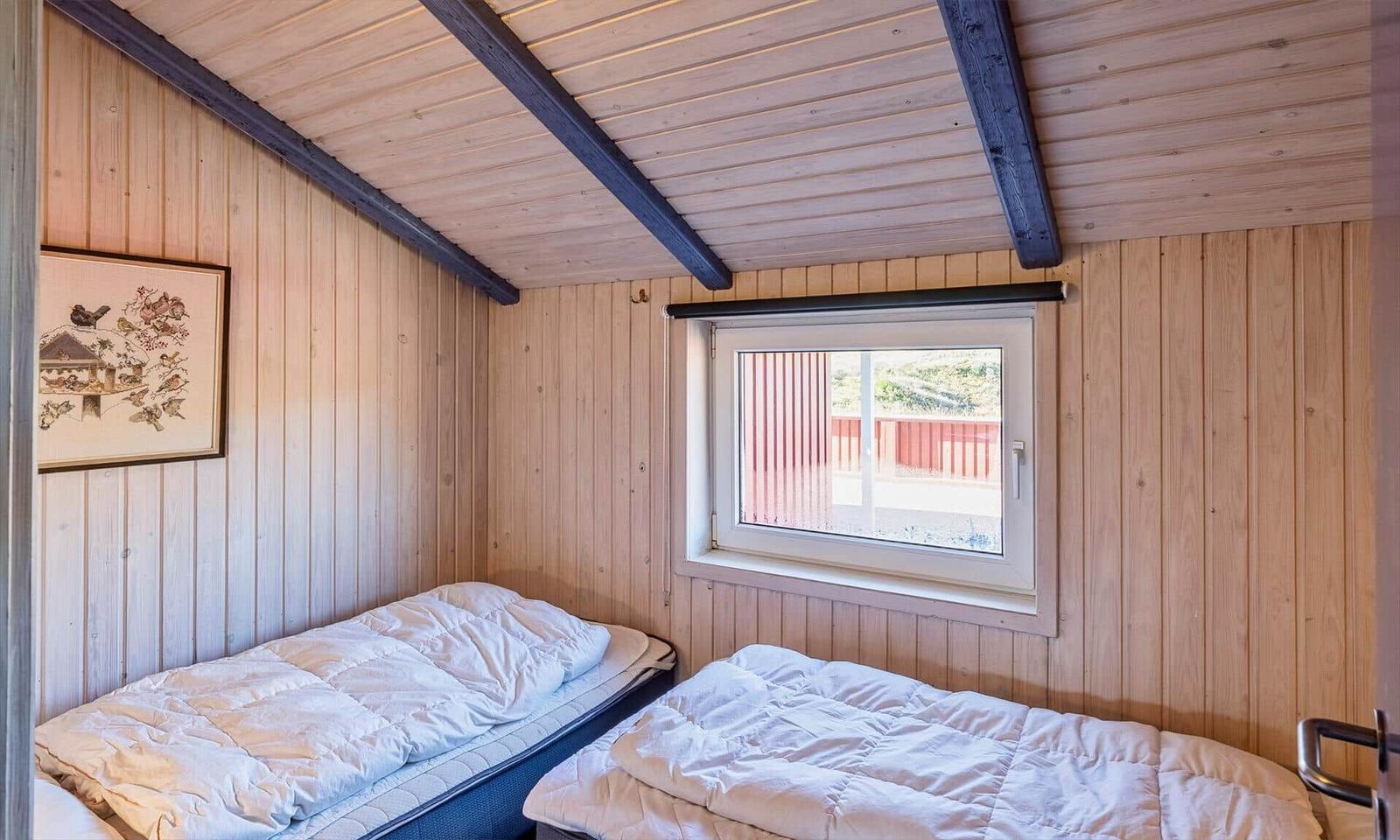 Zwei Betten in einem Holzraum mit Fenster und Deckenbalken.